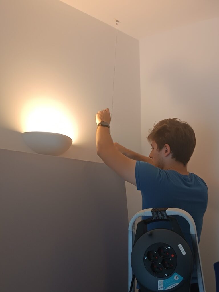 Montaggio di una lampada a parete in regia, in piedi su una scala